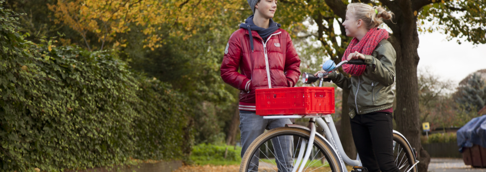 Tiener jongen en meisje praten buiten met elkaar. Meisje heeft een fiets aan de hand.