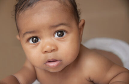 Baby met donkere huidskleur kijkt met grote ogen in de camera