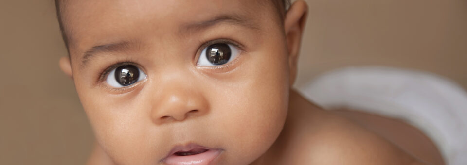 Baby met donkere huidskleur kijkt met grote ogen in de camera