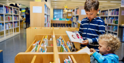 Jongens bekijken in de bibliotheek in Den Haag de boeken om iets te lezen en leren