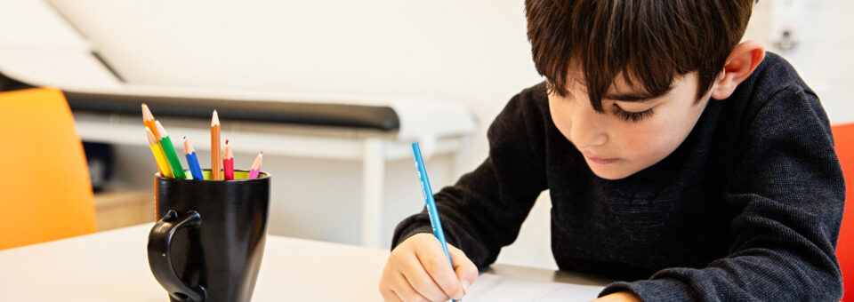 Jongetje krijgt een ontwikkelingsonderzoek bij het CJG en zit te kleuren aan een bureau