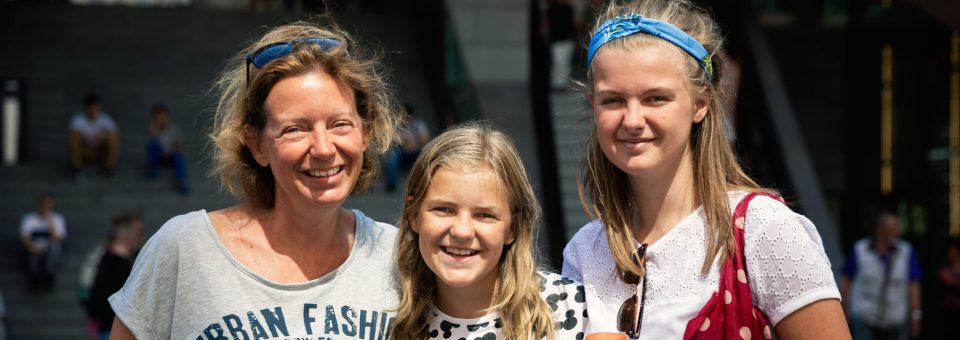 Moeder poseert met haar tiener dochters in de binnenstad van Den Haag. De pubers staan naast hun moeder en ze lachen naar de camera.