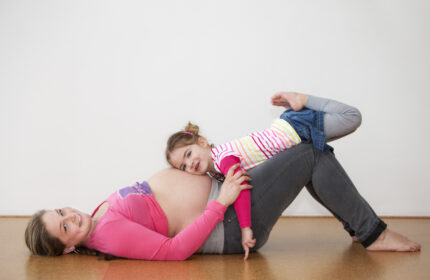 Vrouw in verwachting met dochter die haar hoofd op de zwangere buik heeft liggen
