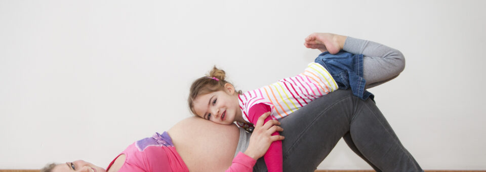 Vrouw in verwachting met dochter die haar hoofd op de zwangere buik heeft liggen