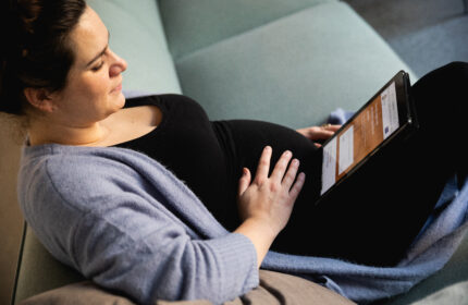 Zijaanzicht van zwangere vrouw met een hand op haar buik die op haar tablet naar de CJG website kijkt