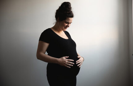 Zwangere vrouw in het zwart gekleed houdt haar handen op haar buik