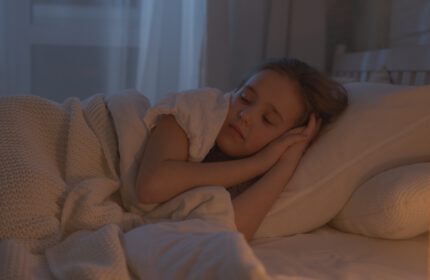 Kind ligt met handen onder haar hoofd en met ogen dicht in bed