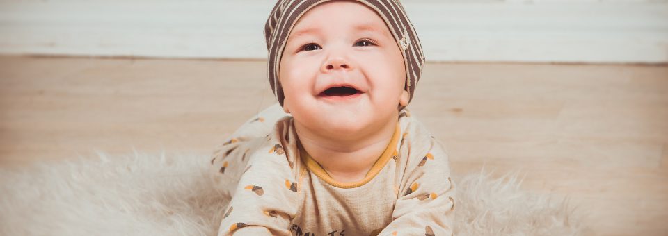 Baby ligt op de buik op een vloerkleed en kijkt lachend omhoog